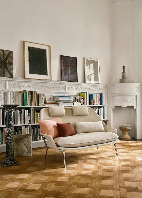 Eleganter Leseraum mit Bücherwand, Parkett und Stuck, beigem Vitra-Sessel, farbigen Kissen und gerahmter Kunst.