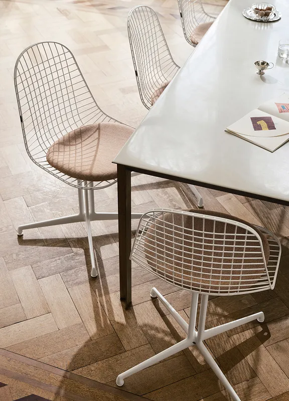Heller Essbereich mit hellen Holzboden, Vitra Wire Chairs in Weiß und Beige. Auf dem Tisch liegt ein offenes Buch und eine kleine silberne Schale.